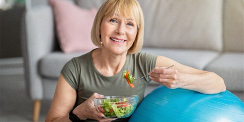 woman eating salad while sitting near exercise ball
